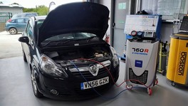 A car with its bonnet up, connected to the air conditioning recharge machine in the workshop